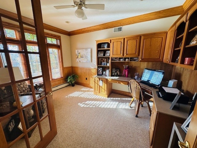 carpeted office with ceiling fan, baseboard heating, crown molding, wood walls, and built in desk