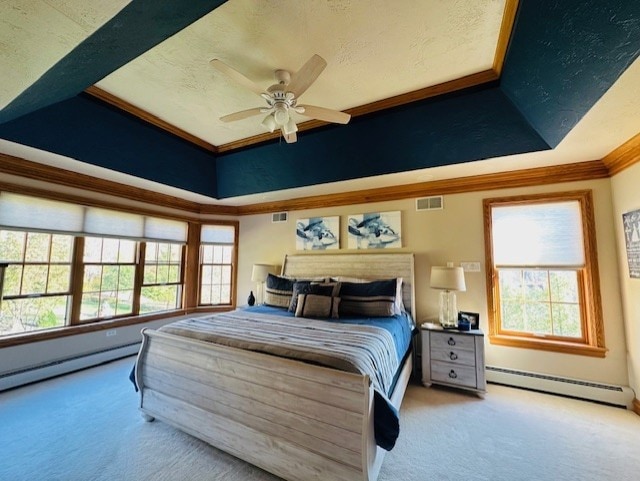 carpeted bedroom with multiple windows, a tray ceiling, baseboard heating, and ceiling fan