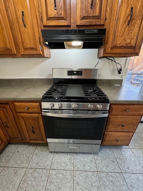 kitchen with decorative backsplash, light tile patterned flooring, and stainless steel gas range oven