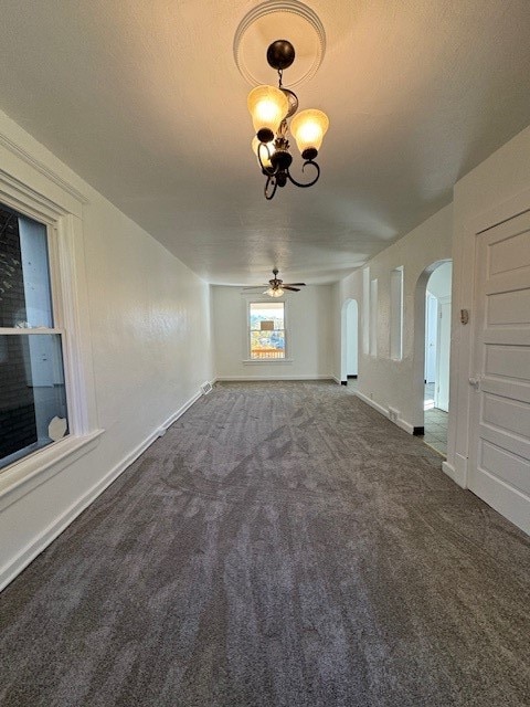 unfurnished living room featuring dark carpet, a textured ceiling, and ceiling fan with notable chandelier