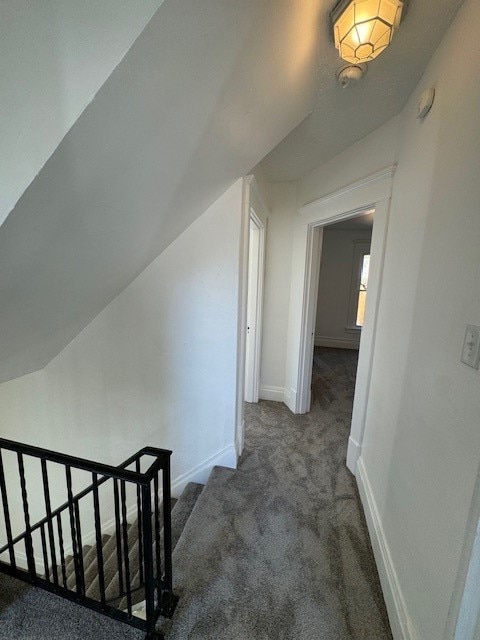 corridor with vaulted ceiling and dark colored carpet