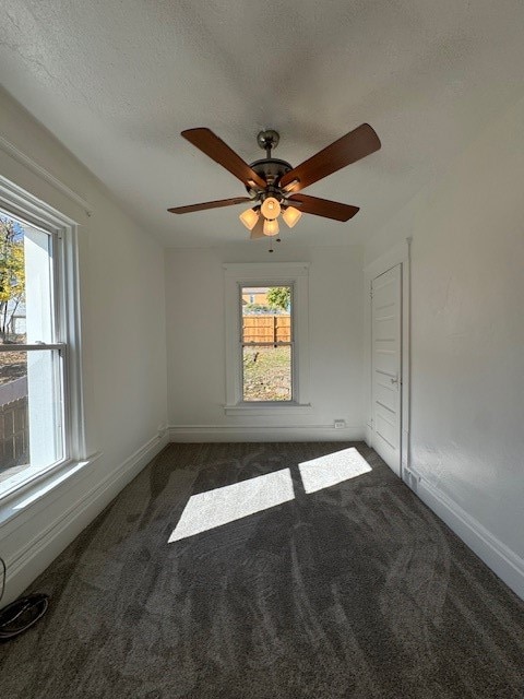 spare room featuring a textured ceiling, ceiling fan, and dark colored carpet