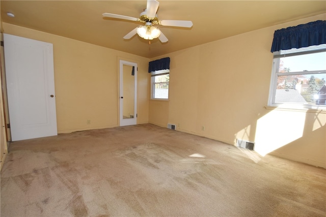 empty room with a wealth of natural light, ceiling fan, and light carpet