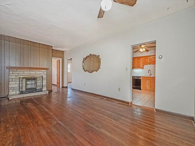 unfurnished living room featuring ceiling fan, light hardwood / wood-style floors, a stone fireplace, and wood walls