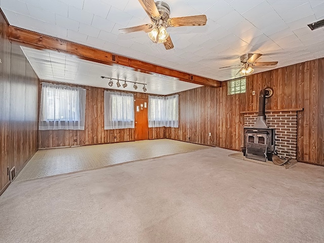 unfurnished living room with a wood stove, beam ceiling, carpet, and ceiling fan