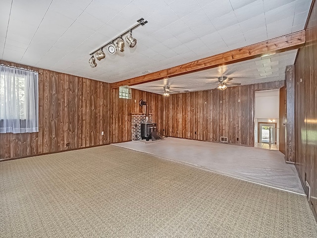 basement featuring carpet, ceiling fan, wood walls, and a wood stove