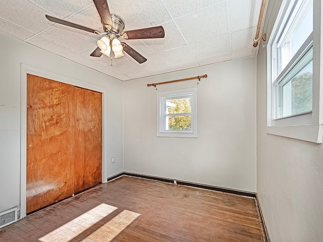 unfurnished bedroom featuring a closet, a paneled ceiling, hardwood / wood-style floors, and ceiling fan