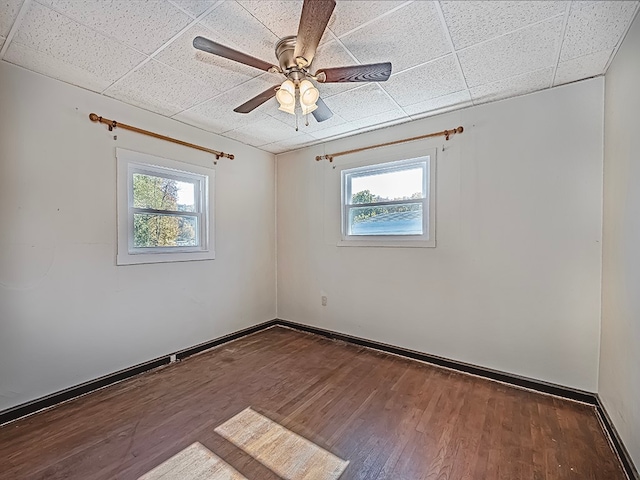 unfurnished room featuring a drop ceiling, plenty of natural light, and dark hardwood / wood-style flooring