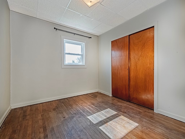 unfurnished bedroom with a closet, hardwood / wood-style floors, and a paneled ceiling