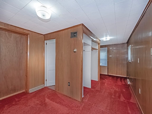 hallway featuring dark carpet and wooden walls