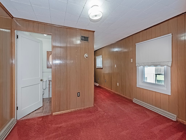 carpeted spare room with wood walls and a baseboard heating unit