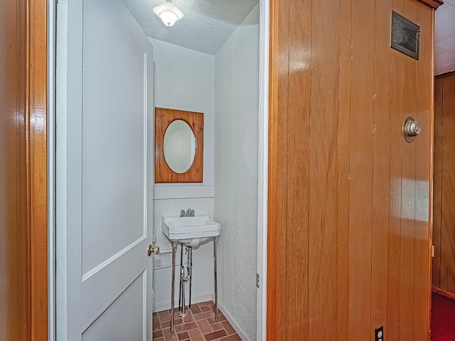 bathroom with a textured ceiling, sink, and wooden walls