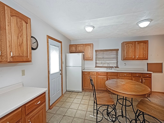 kitchen featuring white fridge, light tile patterned floors, a textured ceiling, and sink