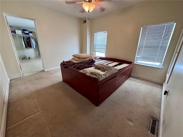 bedroom with multiple windows, ceiling fan, a closet, and light carpet