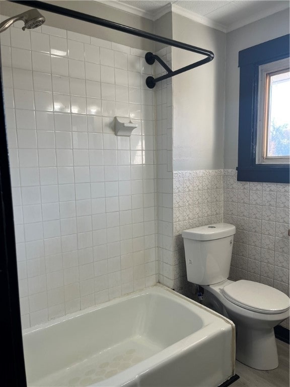 bathroom featuring hardwood / wood-style flooring, crown molding, toilet, tile walls, and tiled shower / bath combo