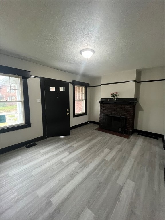 unfurnished living room featuring light wood-type flooring, a textured ceiling, a healthy amount of sunlight, and a brick fireplace