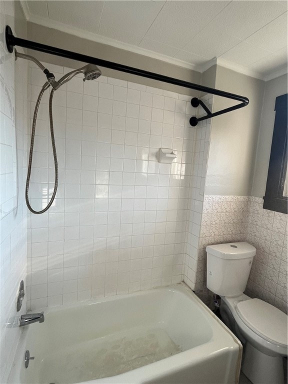 bathroom with tile walls, ornamental molding, toilet, and tiled shower / bath