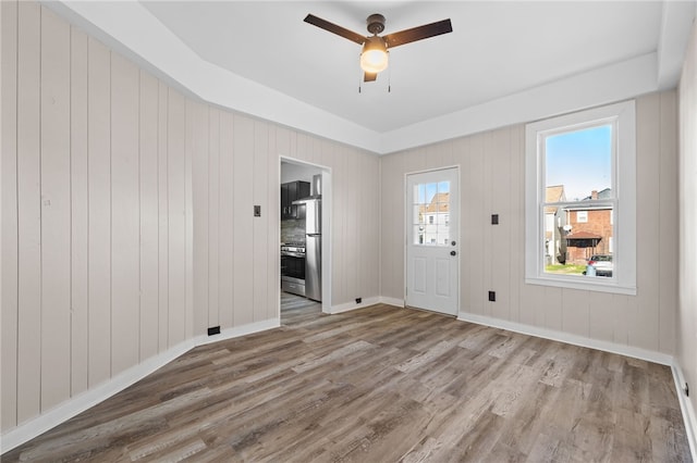 empty room featuring wooden walls, light wood-type flooring, and ceiling fan