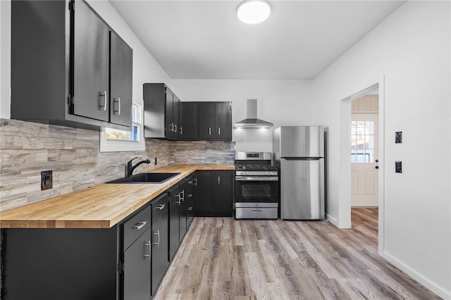 kitchen featuring wall chimney range hood, light hardwood / wood-style flooring, appliances with stainless steel finishes, and a wealth of natural light