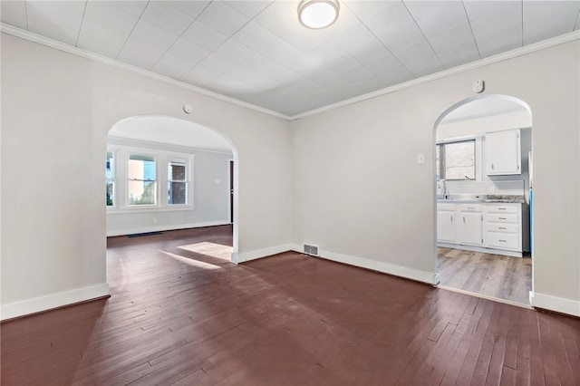 empty room with ornamental molding, a healthy amount of sunlight, and dark wood-type flooring