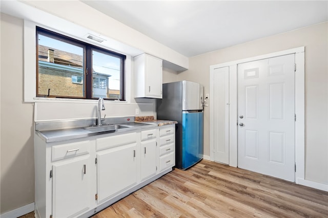 kitchen featuring sink, white cabinets, light wood-type flooring, and stainless steel refrigerator