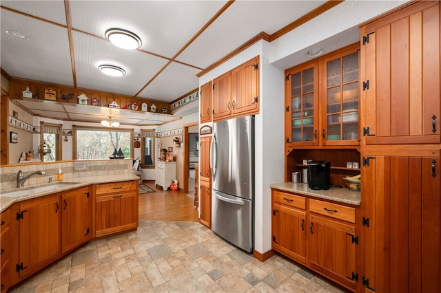 kitchen with crown molding, stainless steel fridge, light stone counters, and sink