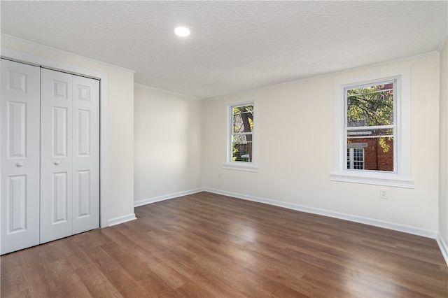 unfurnished bedroom featuring multiple windows, a textured ceiling, a closet, and dark hardwood / wood-style flooring