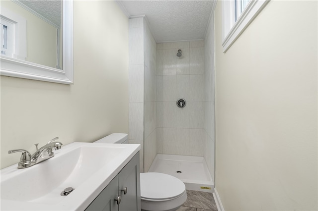 bathroom with toilet, a textured ceiling, vanity, and a tile shower