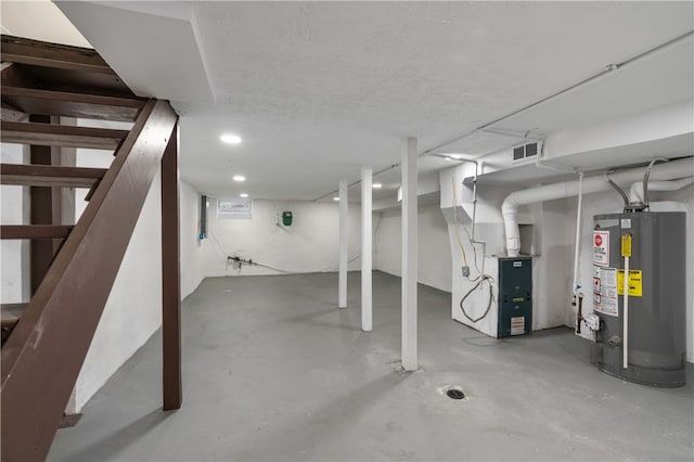 basement featuring water heater, heating unit, and a textured ceiling