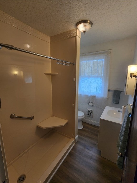 bathroom featuring a textured ceiling, walk in shower, wood-type flooring, toilet, and vanity