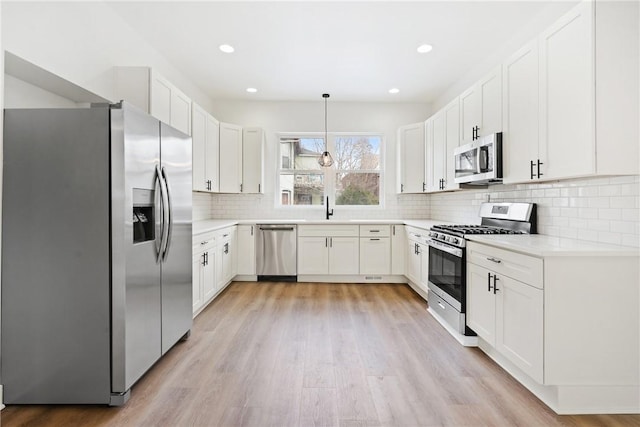 kitchen featuring pendant lighting, sink, light hardwood / wood-style flooring, stainless steel appliances, and white cabinets