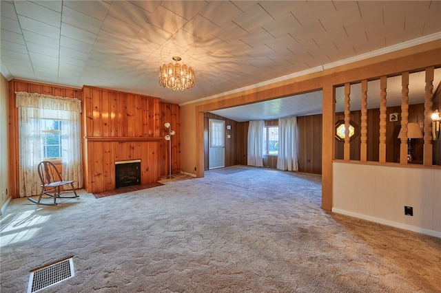 unfurnished living room featuring ornamental molding, wooden walls, carpet, and a wealth of natural light