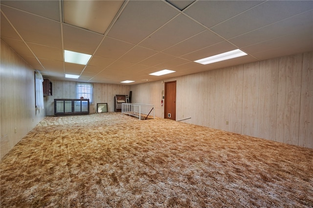 basement with a drop ceiling, wooden walls, and carpet flooring