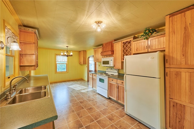 kitchen with wooden walls, hanging light fixtures, sink, a notable chandelier, and white appliances