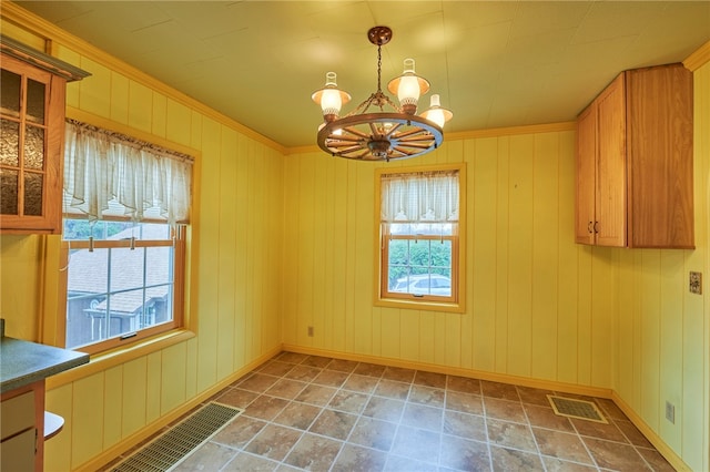 unfurnished dining area featuring ornamental molding, a chandelier, a healthy amount of sunlight, and wooden walls