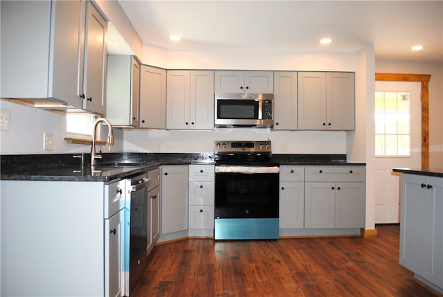 kitchen featuring gray cabinetry, sink, dark hardwood / wood-style flooring, stainless steel appliances, and dark stone counters