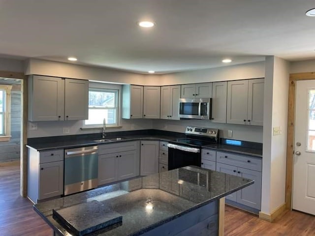 kitchen featuring appliances with stainless steel finishes, dark stone counters, dark wood-type flooring, gray cabinetry, and sink