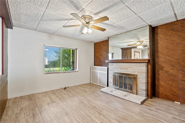 unfurnished living room with light hardwood / wood-style flooring, ceiling fan, and wood walls