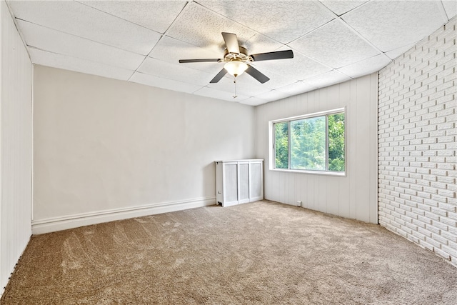 empty room with ceiling fan, brick wall, carpet, and a drop ceiling