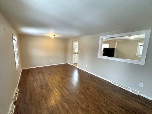 empty room with baseboards, visible vents, and dark wood-type flooring