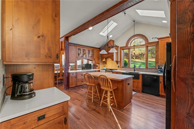 kitchen featuring a kitchen island, hardwood / wood-style floors, vaulted ceiling with skylight, a breakfast bar, and black appliances