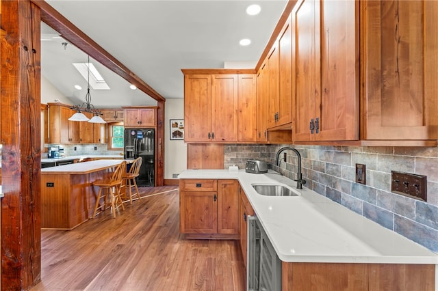 kitchen with hanging light fixtures, black refrigerator with ice dispenser, sink, vaulted ceiling with skylight, and light hardwood / wood-style floors