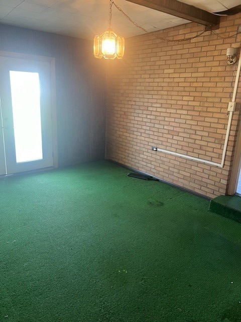 carpeted spare room with beamed ceiling and brick wall