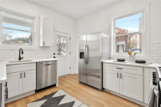 kitchen with appliances with stainless steel finishes, white cabinetry, sink, backsplash, and light hardwood / wood-style floors