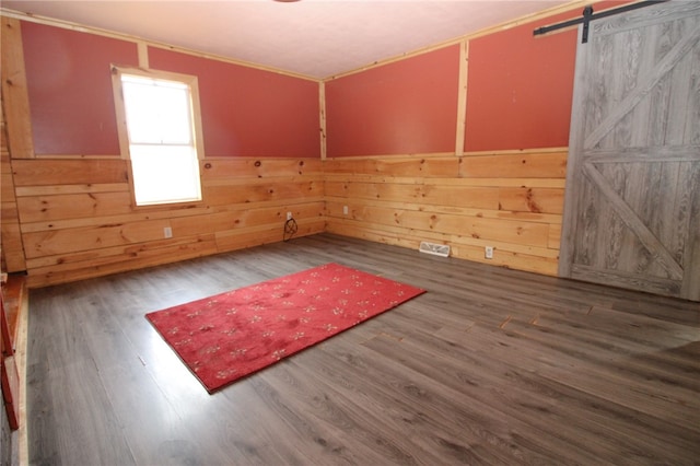 empty room with ornamental molding, a barn door, wood-type flooring, and wood walls