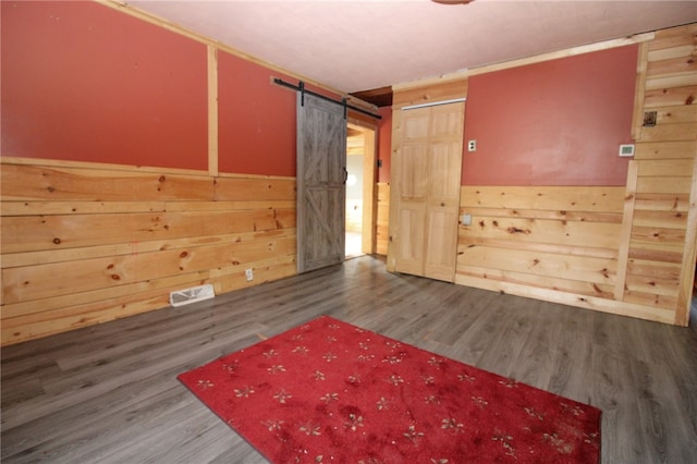 empty room with dark hardwood / wood-style floors, a barn door, and wood walls