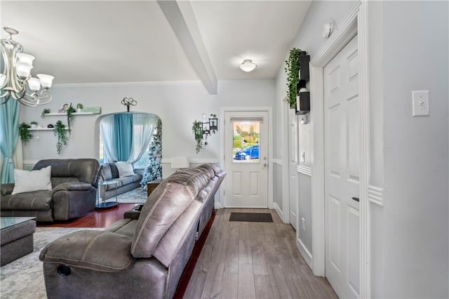 living room with beamed ceiling, a chandelier, wood-type flooring, and ornamental molding