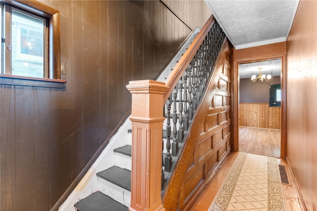 stairway with tile patterned floors, an inviting chandelier, and wood walls