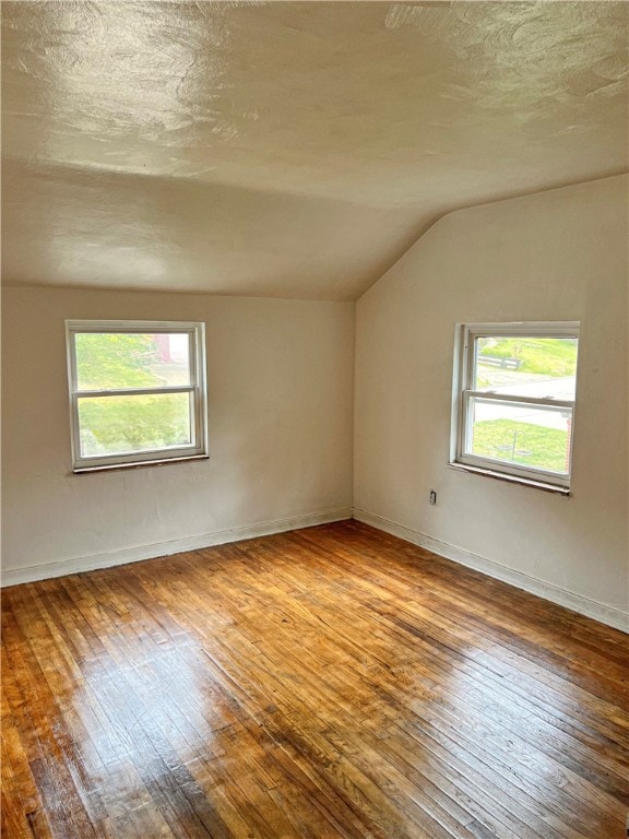 spare room featuring lofted ceiling, hardwood / wood-style floors, a textured ceiling, and plenty of natural light