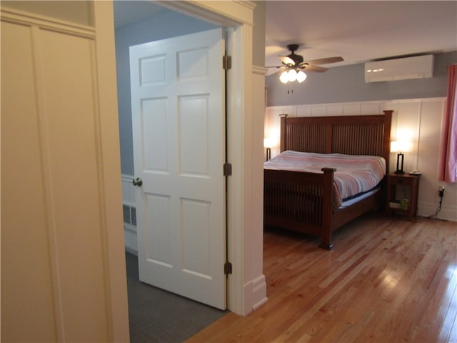 bedroom with hardwood / wood-style floors, ceiling fan, and a wall mounted air conditioner